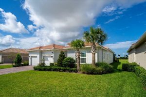 Single-story starter home in Port St. Lucie with palm trees, manicured lawn, and blue sky